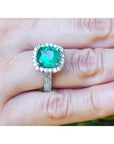 Cushion cut 3.92 ct natural emerald ring with diamond halo and band in 14K white gold on a hand.
