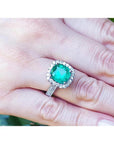Cushion cut 3.92 ct natural emerald ring with diamond halo and band in 14K white gold on a hand.