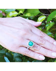 Cushion cut 3.92 ct. natural Colombian emerald ring with diamond halo in 14K white gold on a hand.