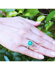 Cushion cut 3.92 ct. natural Colombian emerald ring with diamond halo in 14K white gold on a hand.