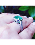 Emerald ring on a hand with a blurred green leafy background.