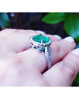 Cushion cut 3.92 ct. natural emerald ring with diamond halo on 14K white gold band, worn on a finger.