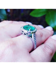 Cushion cut 3.92 ct. natural emerald ring with diamond halo on 14K white gold band, worn on a finger.