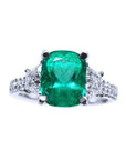 Ring with a cushion cut emerald gemstone and trapezoid diamond accents on each side in white gold.