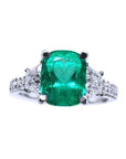 Ring with a cushion cut emerald gemstone and trapezoid diamond accents on each side in white gold.
