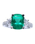 Ring with a cushion cut emerald gemstone and trapezoid diamond accents on each side in white gold.