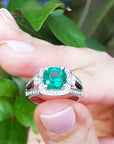 Emerald ring on a finger with a green leafy background.