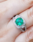 A cushion cut emerald ring on a person's finger.