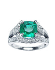 A cushion cut emerald ring topside view on a white background.
