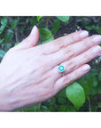 1.45 ct cushion-cut natural emerald ring with diamond halo on a hand, 14K gold band.