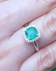 A women's cushion cut halo diamond emerald ring on a person's finger.