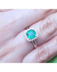 A women's cushion cut halo diamond emerald ring on a person's finger.