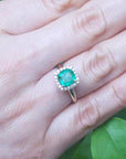 Emerald ring on a hand with a green leafy background.