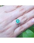 Emerald ring on a hand with a green leafy background.
