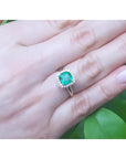 1.45 ct natural cushion-cut emerald ring with diamond halo on a woman's hand.
