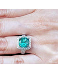 Cushion cut 3.68 ct Colombian emerald engagement ring with diamond halo in 18K white gold on a hand.