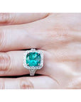 Cushion cut 3.68 ct Colombian emerald engagement ring with diamond halo in 18K white gold on a hand.