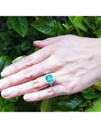 Hand wearing a ladies emerald cushion cut ring with a leafy background.