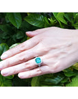 Cushion cut emerald engagement ring with diamond halo in 18K white gold on a hand.