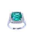 A cushion cut emerald white gold ring for women displaying a halo of natural diamond.