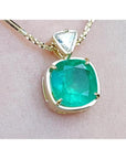 A genuine colombian emerald pendant with 18k yellow gold setting on a light skin background.