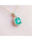 A natural emerald gemstone pendant on a gold chain against a light pink background.