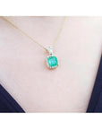 Gold necklace with a natural emerald pendant on a person wearing a black top.