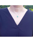 Cushion-cut emerald pendant with halo natural diamonds on a 14K yellow gold chain, worn on a model.