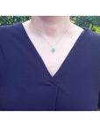 Cushion-cut emerald pendant with halo natural diamonds on a 14K yellow gold chain, worn on a model.