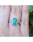 A cushion cut natural colombian emerald ring made of 14k white gold on a finger.