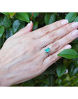 14K white gold cushion-cut emerald solitaire ring with rope detailing on a hand against green leaves.