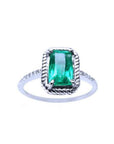 A cushion cut emerald ring may's birthstone in white gold encircled with rope like frame design.