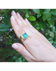 Men's 18k yellow gold ring with a cushion-cut emerald and channel-set diamond accents.