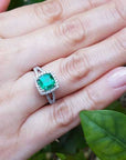 Hand wearing a cushion cut colombian emerald ring against a natural background.