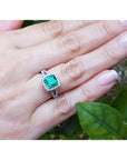 Hand wearing a cushion cut colombian emerald ring against a natural background.