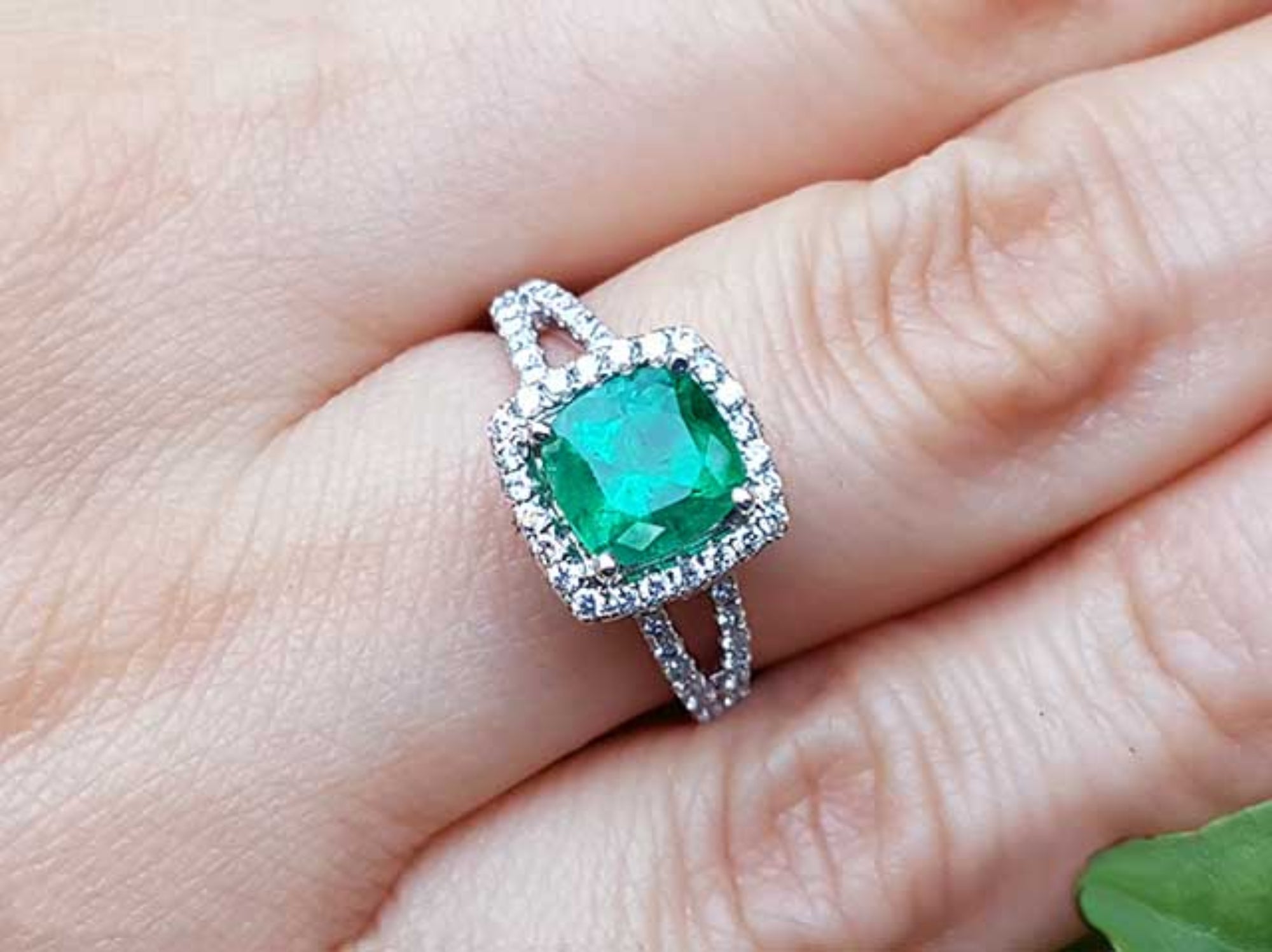 A natural emerald cushion cut in a halo diamond with sides split shank on a finger.
