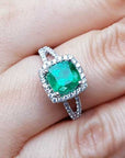 A natural emerald cushion cut in a halo diamond with sides split shank on a finger.