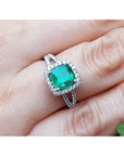 A natural emerald cushion cut in a halo diamond with sides split shank on a finger.