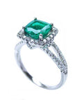 A colombian emerald cushion cut on top of the white gold ring with diamond accents, side split shank profile view.