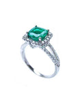A colombian emerald cushion cut on top of the white gold ring with diamond accents, side split shank profile view.