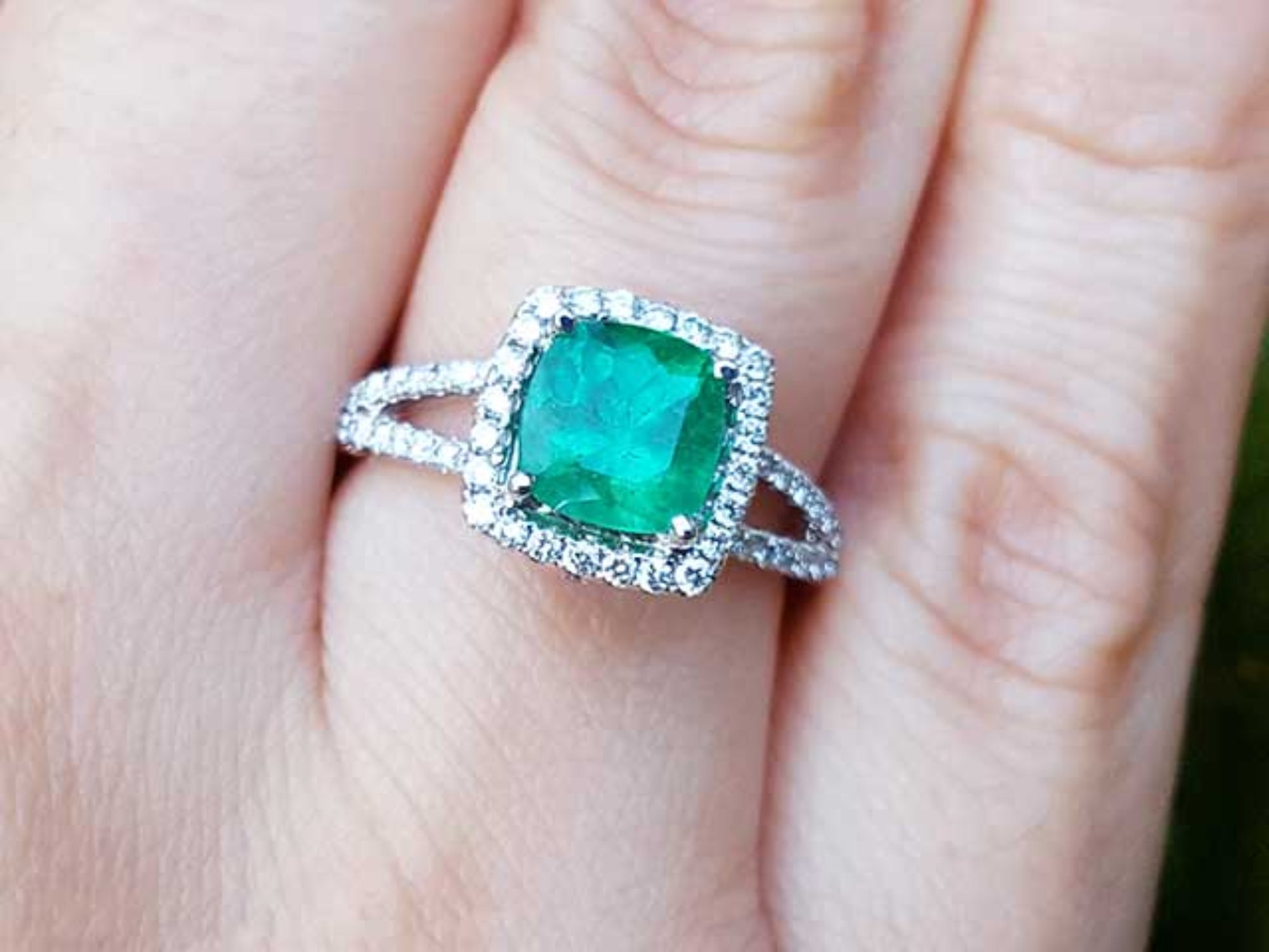 A cushion cut emerald ring with halo diamond on a person's finger.