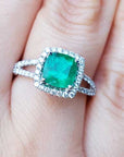 A cushion cut emerald ring with halo diamond on a person's finger.