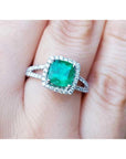 A cushion cut emerald ring with halo diamond on a person's finger.