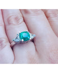 2.18 ct cushion cut emerald ring with trillion side diamonds in 14K white gold on a hand.