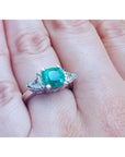 2.18 ct cushion cut emerald ring with trillion side diamonds in 14K white gold on a hand.
