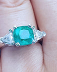Emerald ring with trillion side diamond accents on a finger.