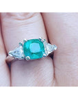 Emerald ring with trillion side diamond accents on a finger.