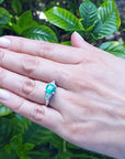 Hand wearing a genuine emerald and trillion side diamond rings for women with a leafy background.