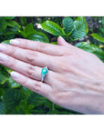 Cushion cut emerald ring with trillion side diamonds in 14K white gold on a hand.