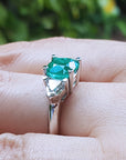 Emerald ring on a hand with a blurred green background.